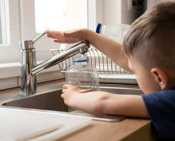 Child filling a water bottle at a kitchen sink