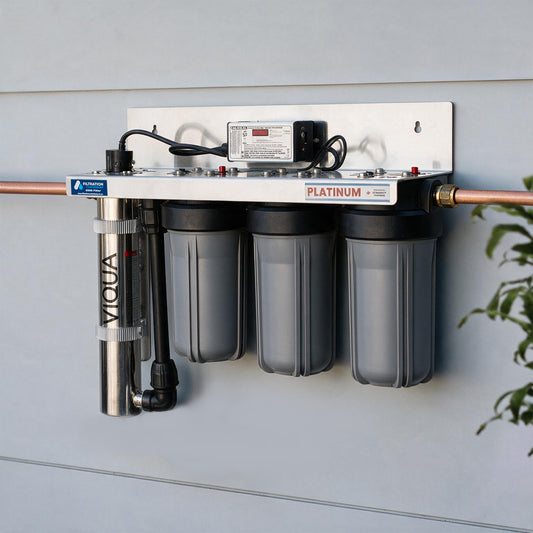 A wall-mounted water filtration system with three gray filter canisters, a copper pipe connection, a vertical stainless steel pre-filter, and a power supply on a white backplate against a light gray wall.