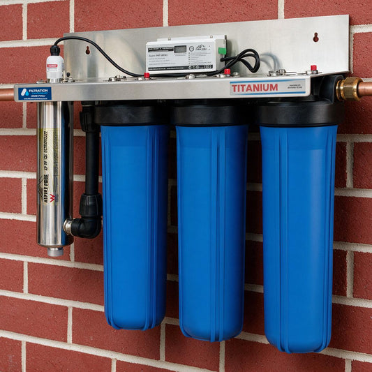 A wall-mounted water filtration system with three large blue filter canisters, a stainless steel control box, and a separate silver cylindrical cartridge, mounted on a red brick wall.